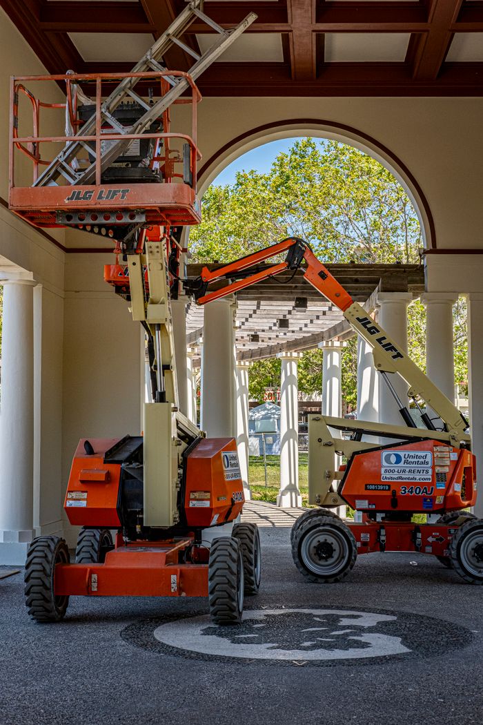 Home 1 Two orange JLG lifts inside a building with a view outside through an archway.