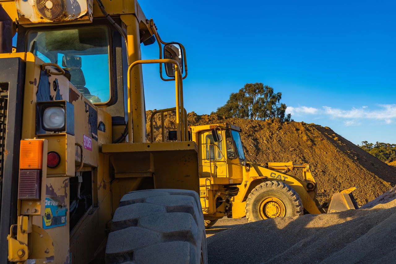 Industrial machinery operating outdoors, showcasing a bulldozer and a loader amidst piles of soil.