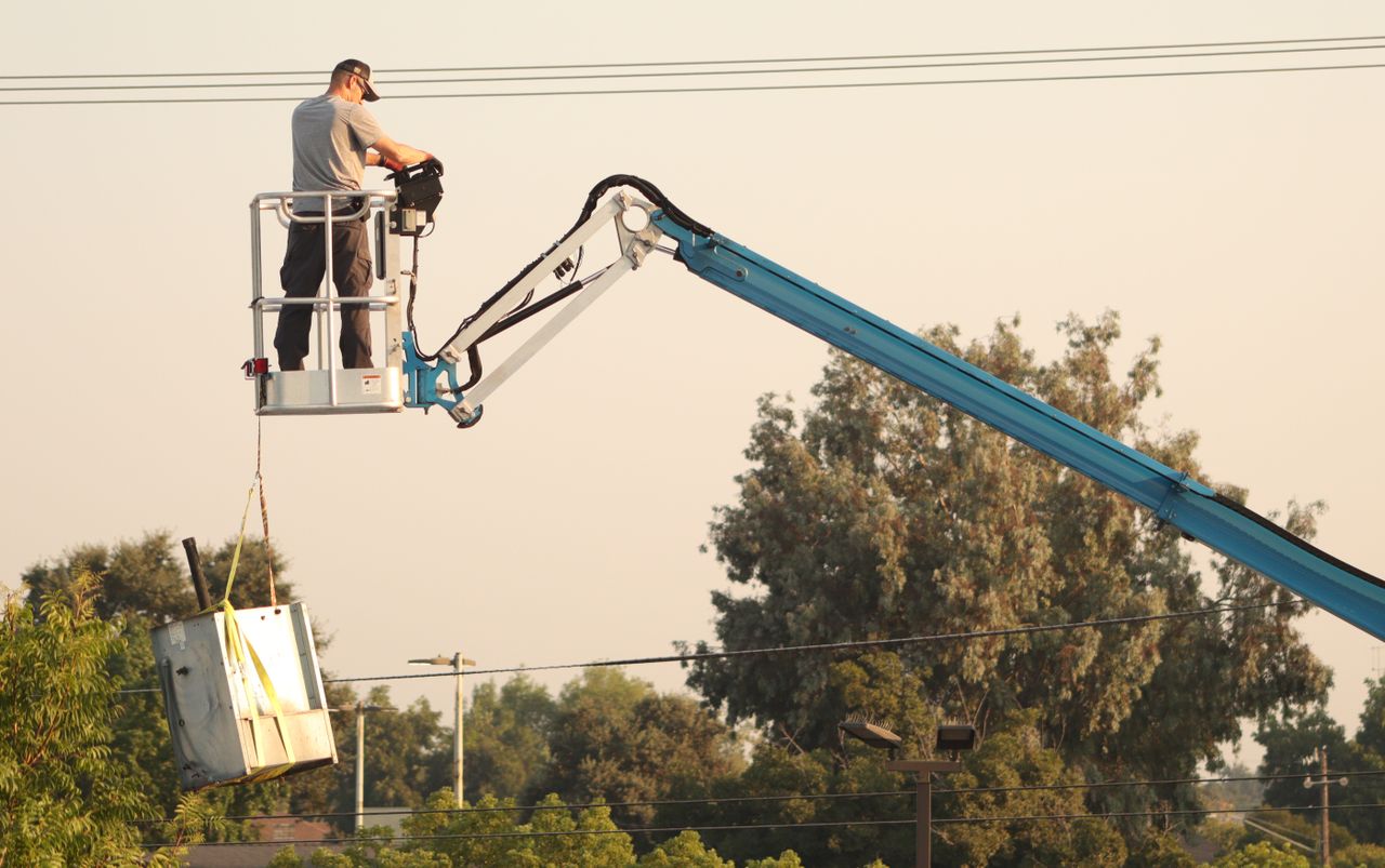 Home 3 Man in a cherry picker operating machinery outdoors, with trees and equipment.