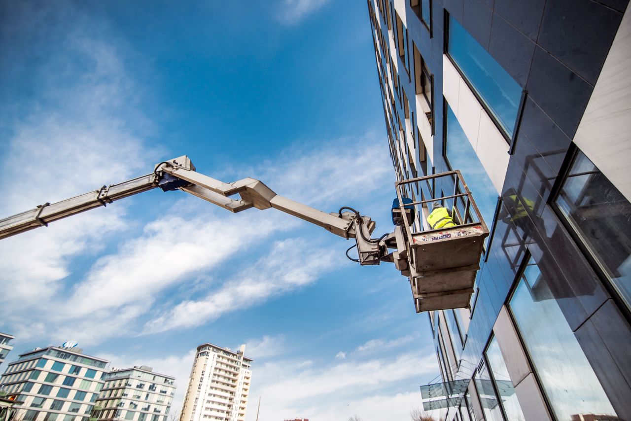 Construction worker on a lift near high-rise building against blue sky.